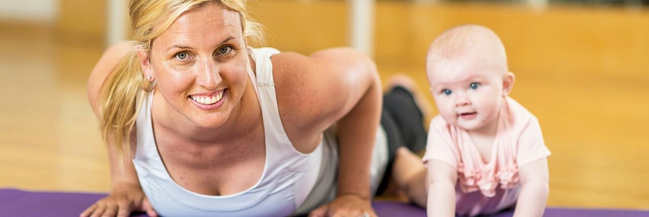 Mutter liegt mit Baby auf Yogamatte